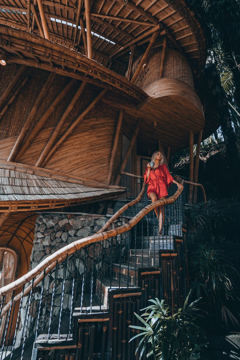 Woman in a red dress descending bamboo stairs of a unique house in Bali.